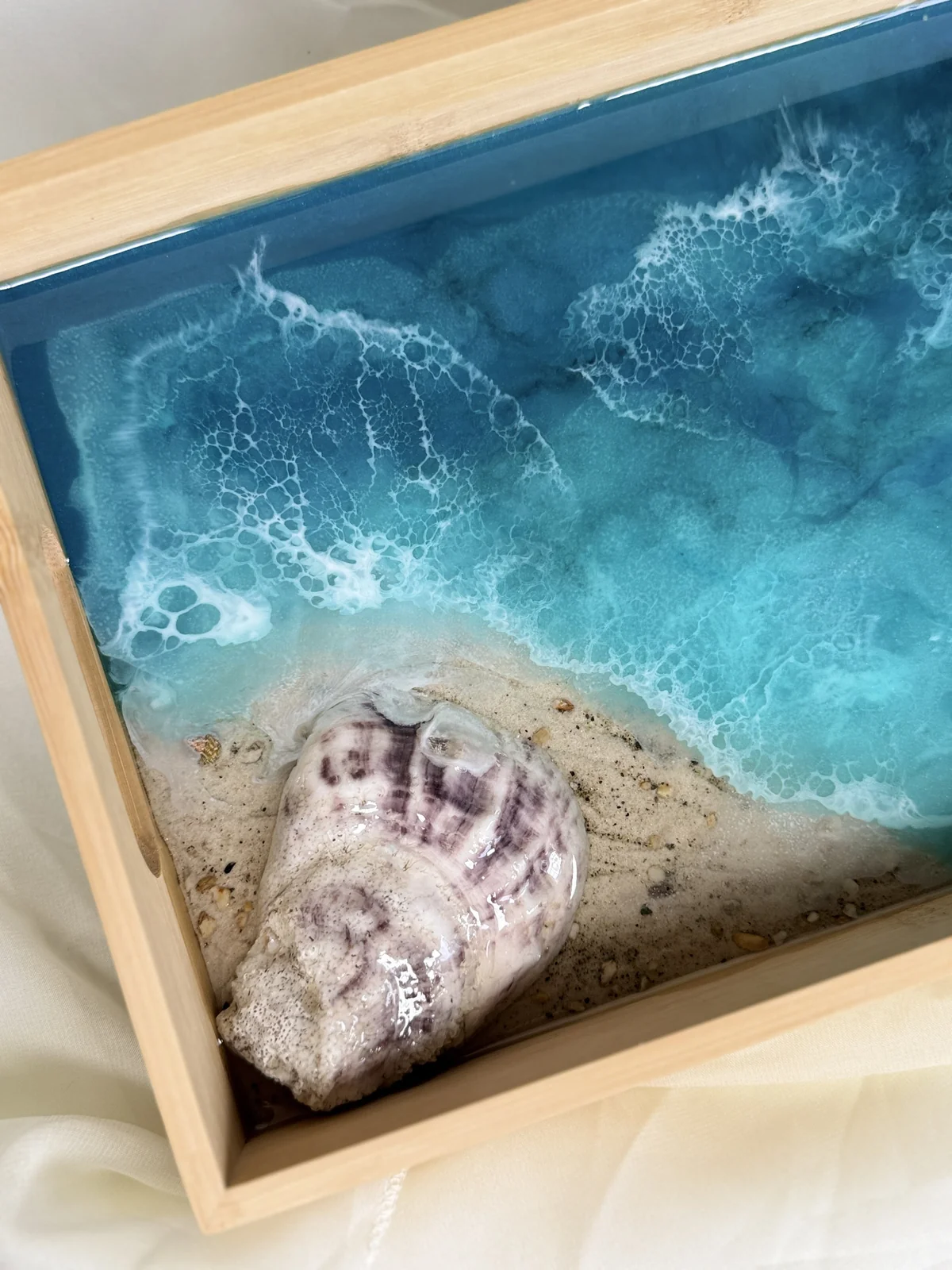 Miniature beach scene in a wooden frame with a shell, sand, and ocean water.
