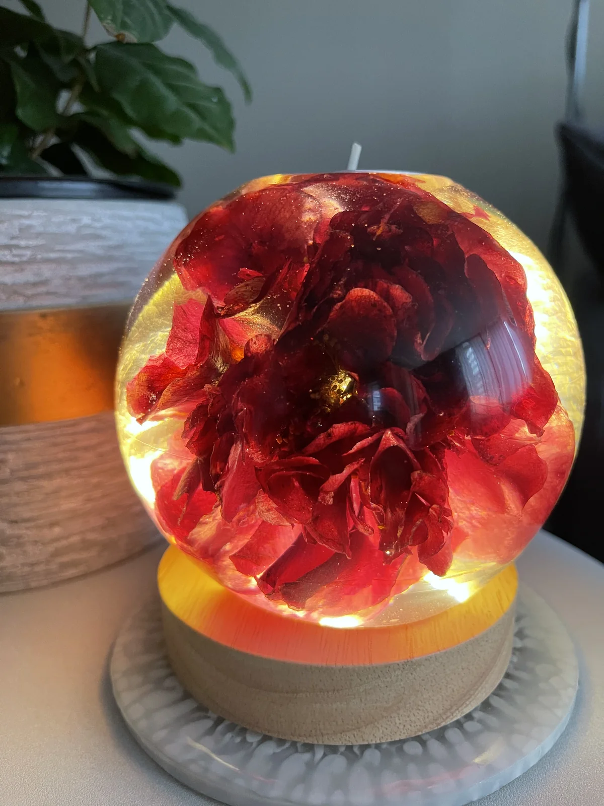 Decorative glass orb with red flower petals inside, illuminated from within, resting on a wooden base.