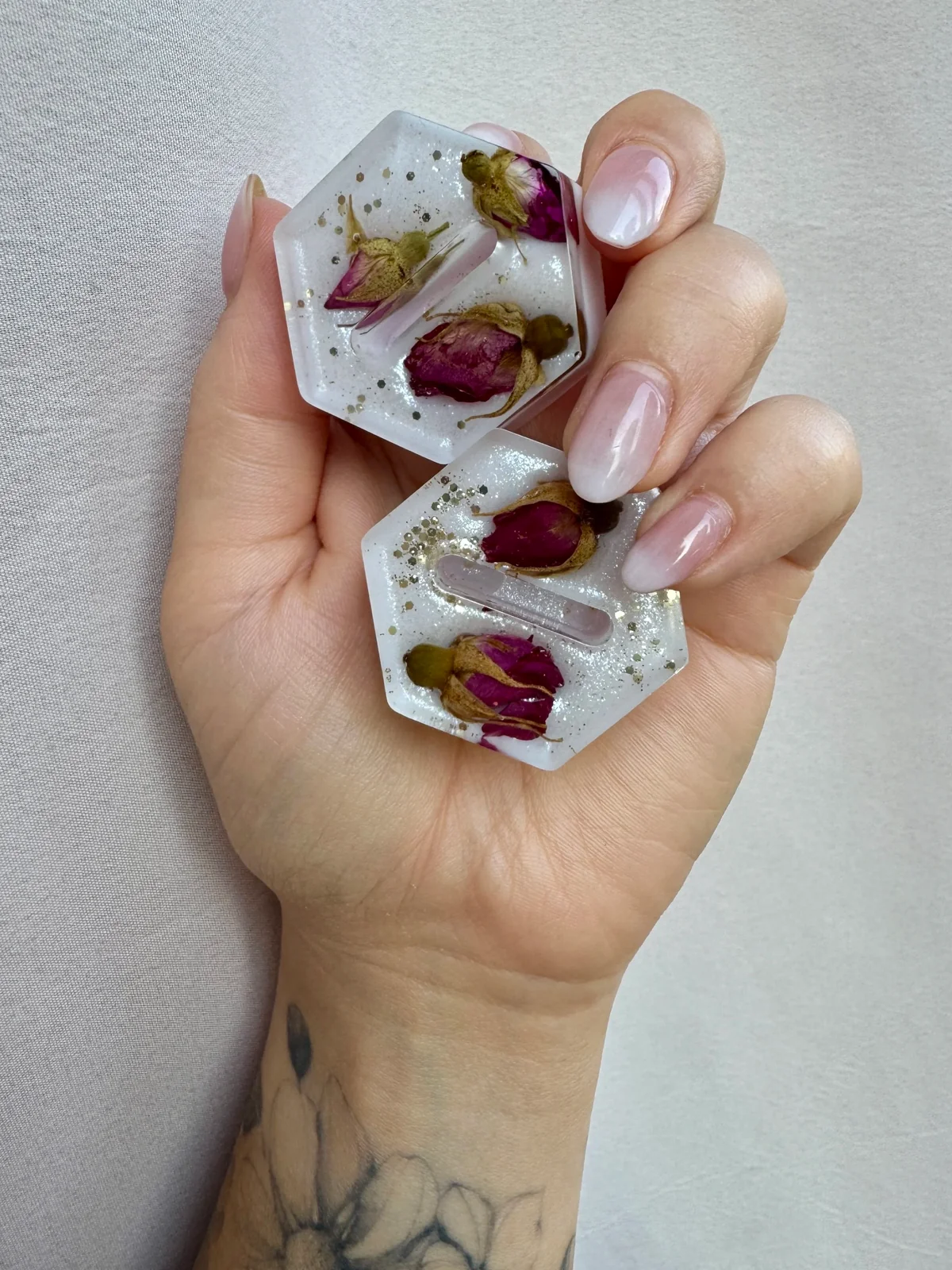 Hand holding two ring holders with dried rosebuds and gold glitter inside.