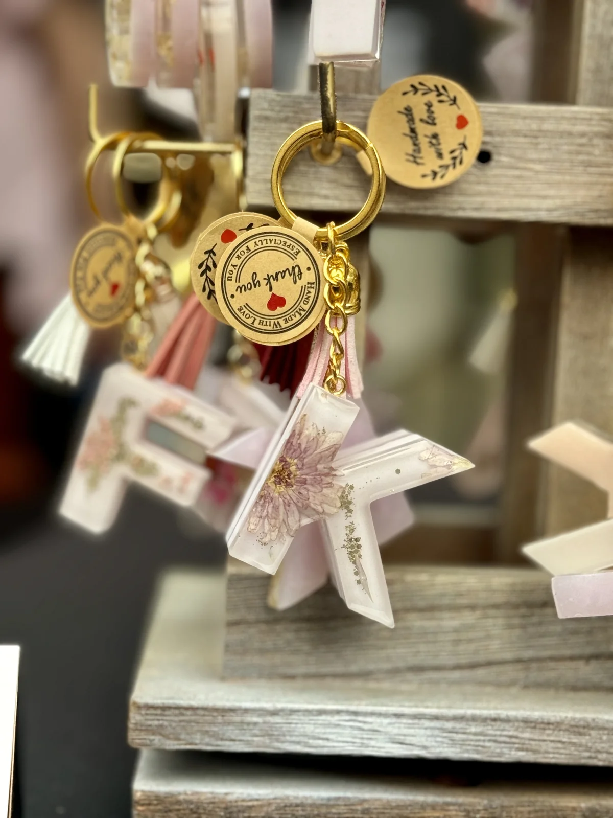 Decorative star-shaped resin keychain with floral design, hanging from a display rack along with gold rings and circular tags with inspirational messages.