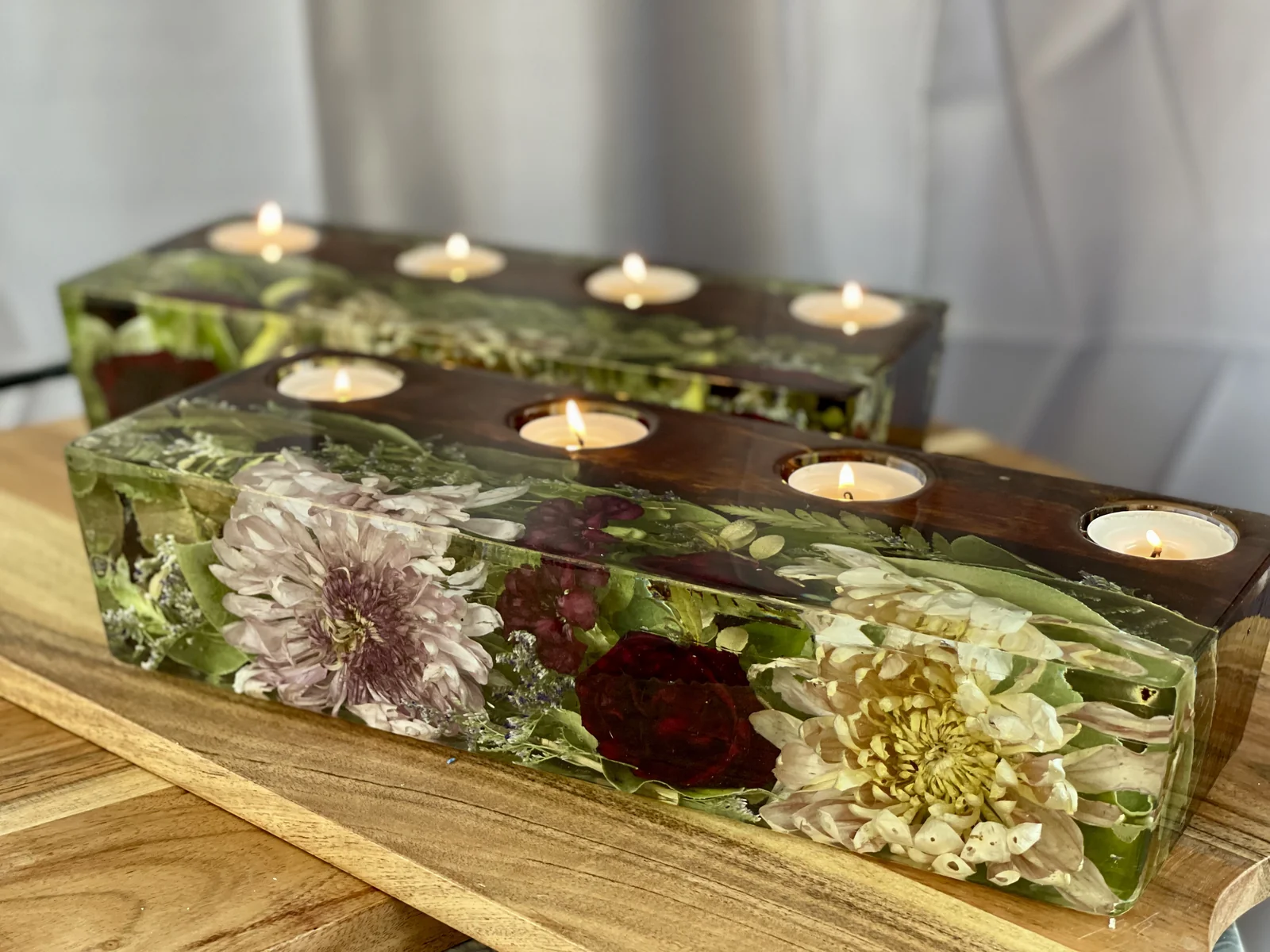 Two rectangular floating floral arrangements with lit tea light candles inside glass containers, placed on a wooden surface.