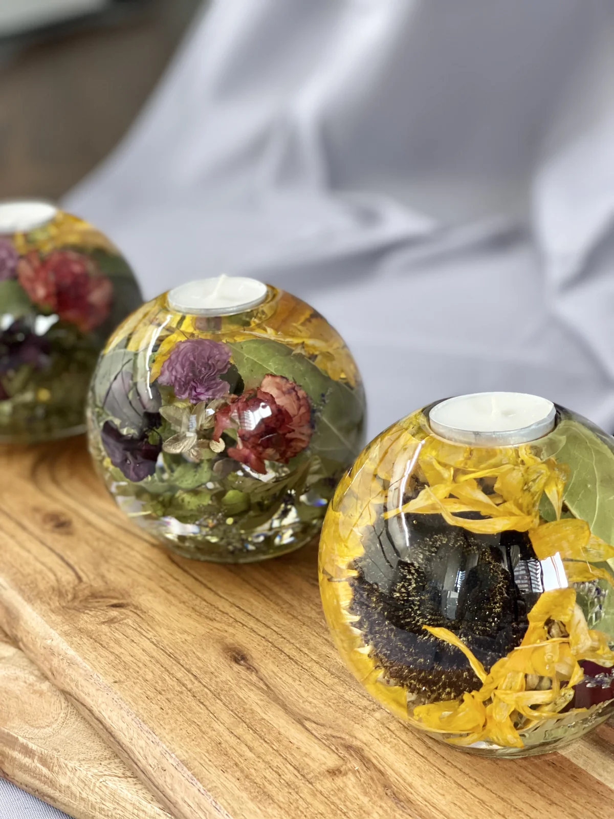 Three round resin candle holders with floral arrangements inside, placed on a wooden surface.
